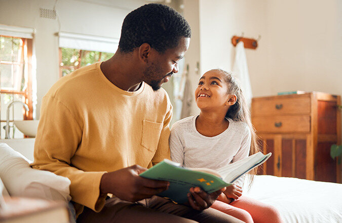 Father and daughter sitting side by side reading together.